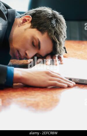 Side profile of a businessman resting his head on a desk in front of a laptop Stock Photo