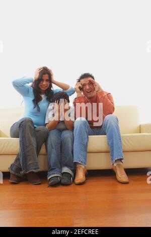 Mid adult man and a young woman with their son watching TV in fear Stock Photo