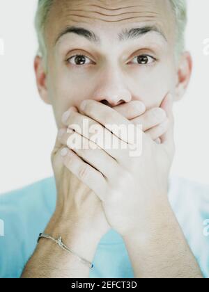 Portrait of a young man covering his mouth with his hands Stock Photo