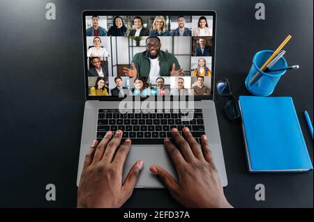 Online business meeting. Multiracial business people working from home by a video conference. Top view at a laptop screen with webcam shots of diverse people and hands of a black man on a keyboard Stock Photo