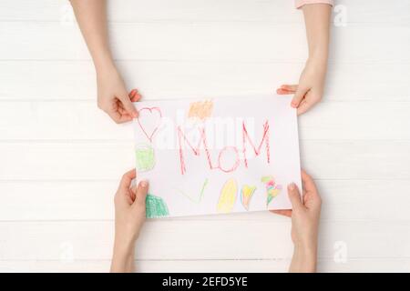 Mom and daughter hands holding colorful DIY postcard with word Mom written on it. Lovely handmade card for mothers day or March 8 ot birthday Stock Photo