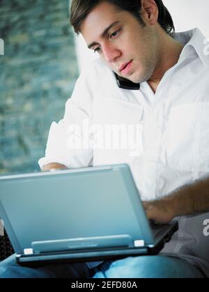 Young man using a laptop while talking on a mobile phone Stock Photo