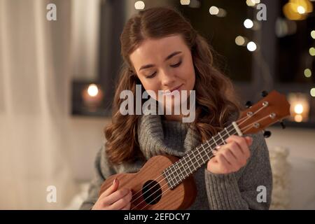 happy young woman playing ukulele guitar at home Stock Photo