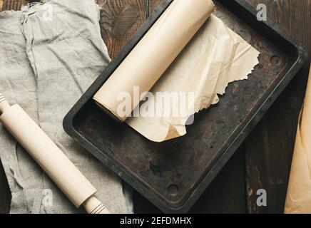 empty rectangular metal pan covered with brown parchment paper and paper rolls on a wooden table, top view Stock Photo