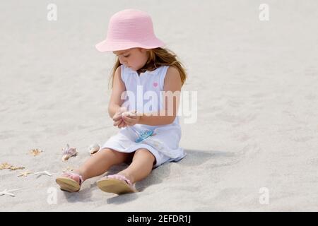Girl sitting near a starfish and seashells on the beach