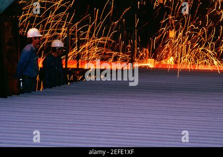 Side profile of two foundry workers standing in a steel mill
