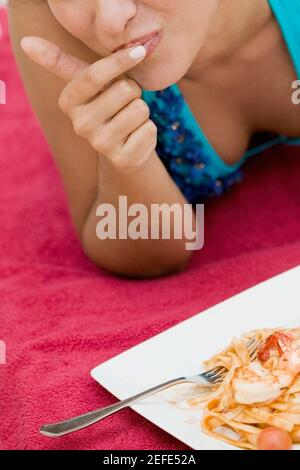 Close-up of a young woman with her finger on her lips and a plate of pasta in front of her Stock Photo