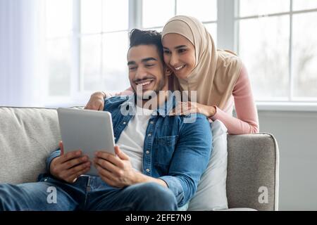 Attractive muslim couple bearded guy and young lady in hijab having video conference via digital tablet while staying home during covid-19 pandemic, m Stock Photo