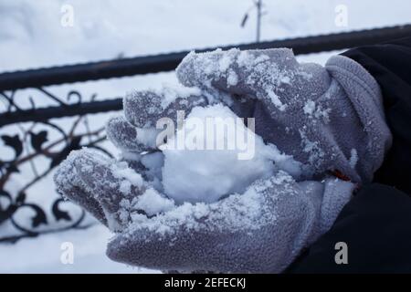 Close up woman hand holding snow. Cold and snowy weather. Winter concept. The woman is wearing gray gloves. Stock Photo