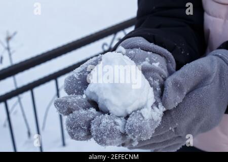 Close up woman hand holding snow. Cold and snowy weather. Winter concept. The woman is wearing gray gloves. Stock Photo