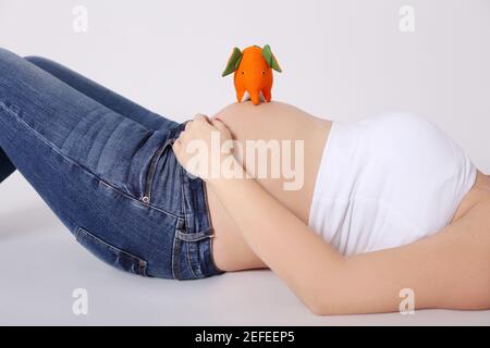 Pregnant woman lying with orange elephant toy, wearing casuail jeans and white top
