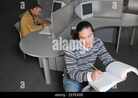 Two young men sitting in a computer lab and writing Stock Photo