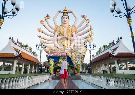 KOH SAMUI, THAILAND - January 10, 2020: Woman in a red dress standing in front of statue of Shiva in Wat Plai Laem Temple on Koh Samui island in Stock Photo