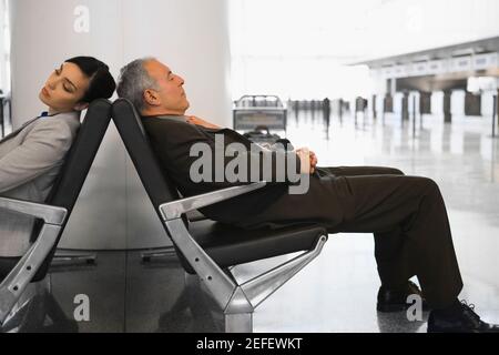 Businessman and a businesswoman sleeping on chairs at an airport Stock Photo