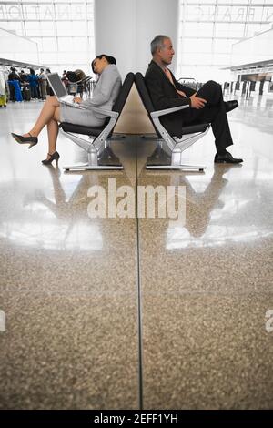 Side profile of a businessman and a businesswoman sitting at an airport lounge Stock Photo