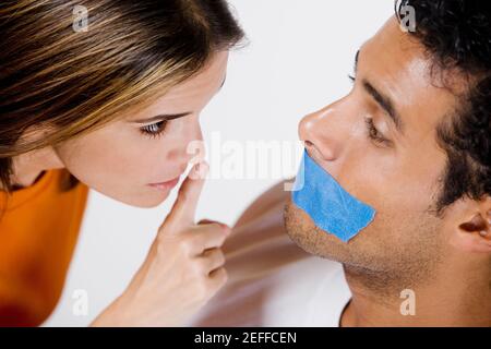 Young man with adhesive tape on his mouth and mid adult woman looking at him Stock Photo