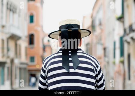 Rear view of a gondolier standing wearing a hat, Venice, Veneto, Italy Stock Photo
