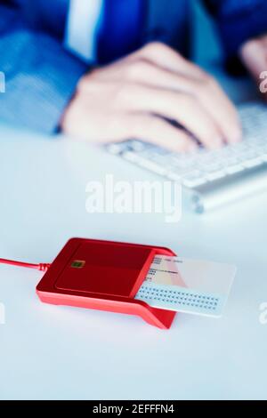 an electronic identification in a red reader on a white front desk, and a young caucasian man, wearing an elegant blue suit sitting at this desk Stock Photo