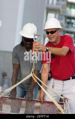 Two manual workers fastening a container in the hook of a lift Stock Photo