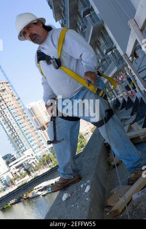 Mature man standing at the edge of a building and holding a hammer Stock Photo