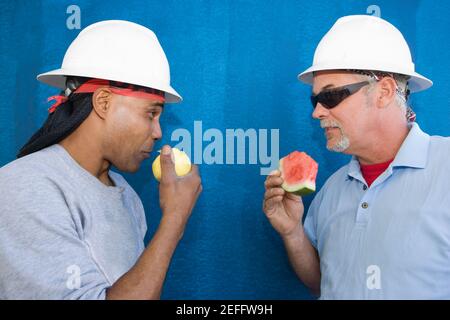 Close-up of two male construction workers face to face and eating fruits Stock Photo