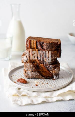 Banana bread cut into slices in stack with glass of milk on plain gray concrete background. Selective focus. Stock Photo
