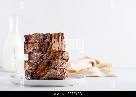 Banana bread cut into slices in stack with glass of milk on plain gray concrete background. Selective focus. Stock Photo