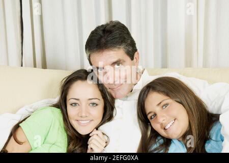 Portrait of a mature man sitting with his two daughters on a couch and smiling Stock Photo