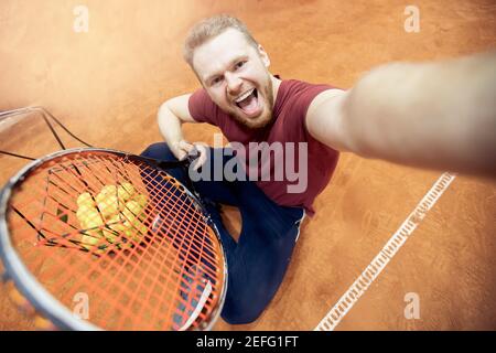 Smiling man tennis trainer player with racket and ball on court. Stock Photo