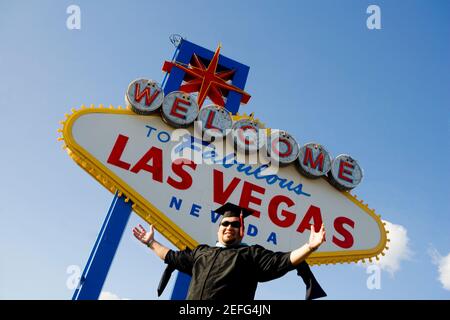 Low angle view of a young man standing in font of a Las Vegas sign board, Las Vegas, Nevada, USA Stock Photo