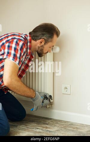 Quality help. Handyman using pipe wrench while repairing radiator battery in the room. Heating restoration Stock Photo