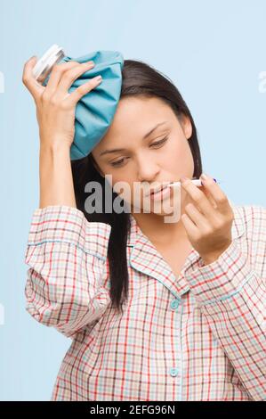 Close-up of a young woman measuring her temperature with a thermometer and holding an ice pack on her head Stock Photo