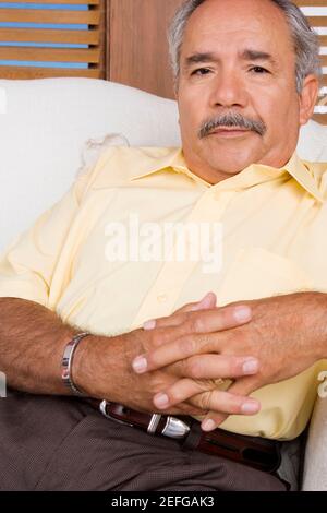 Portrait of a senior man sitting on a couch with his hands clasped Stock Photo
