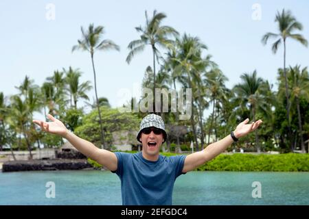 Young man standing with his arms outstretched and shouting, Captain CookÅ½s Monument, Kealakekua Bay, Kona Coast, Big Island, Hawaii islands, USA Stock Photo