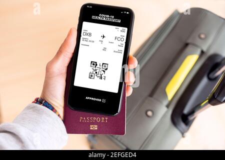 Overhead view of an human hand holding a passport and a smart phone with a digital health passport with a boarding pass Stock Photo