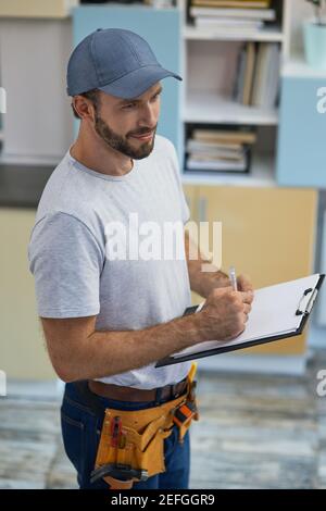 Quality service. Professional young repairman making notes on clipboard while standing indoors Stock Photo