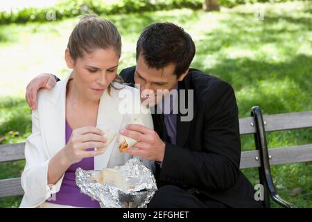 Businessman and a businesswoman having food on a park bench Stock Photo