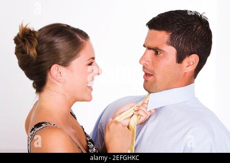 Side profile of a young woman pulling a mid adult man with his tie Stock Photo