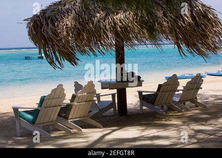 Beach chairs under palapa on the beach, Coral Cay, Dixon Cove, Roatan, Bay Islands, Honduras Stock Photo