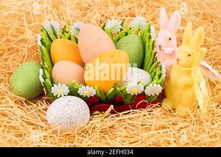 Easter colorful eggs in basket and bunnies on straw background. Stock Photo