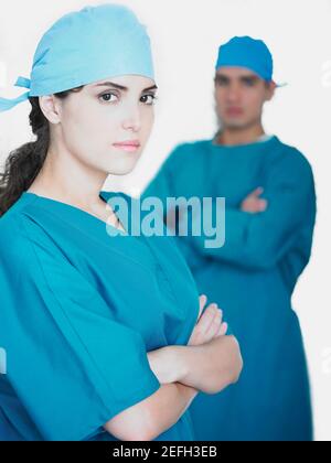 Portrait of a female doctor standing with her arms crossed and a male doctor standing in the background Stock Photo
