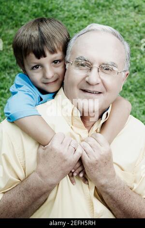 Portrait of a senior man giving a piggyback to his grandson and smiling Stock Photo