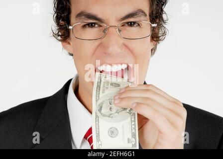 Portrait of a businessman putting a dollar bill into his mouth Stock Photo