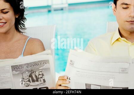 Close-up of a young couple reading newspapers at the poolside Stock Photo