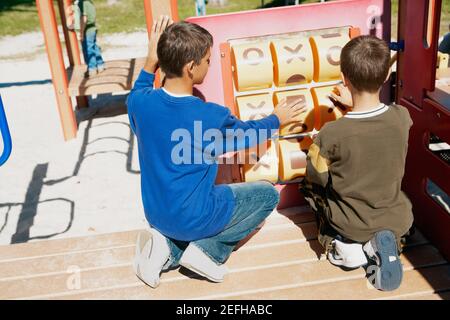 Rear view of a teenage boy and a boy playing tic tac toe Stock Photo