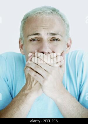 Portrait of a young man covering his mouth with his hands Stock Photo