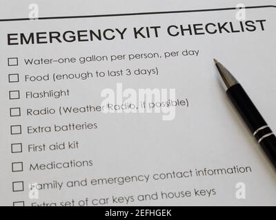 An emergency kit checklist printed on white paper and ink pen are shown close. Stock Photo
