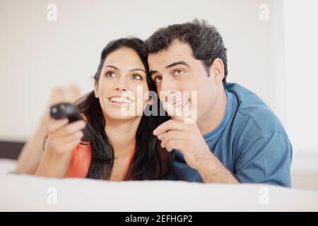 Close up of a young woman and a mid adult man lying on the bed and watching television Stock Photo