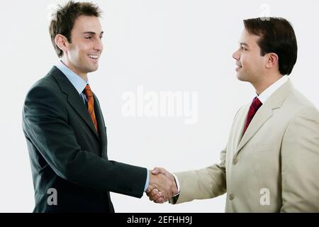 Side profile of two businessmen shaking hands and smiling Stock Photo