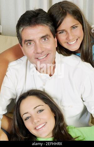 Portrait of a mature man and his two daughters sitting on a couch and smiling Stock Photo
